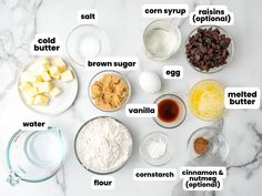 the ingredients to make chocolate chip cookies laid out on a white marble counter top, including eggs, raisins, butter, and sugar