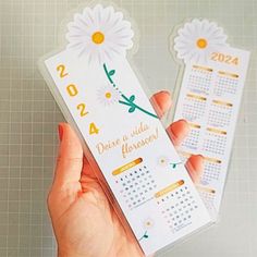 a person holding two calendar stickers in their left hand, one with a daisy on it