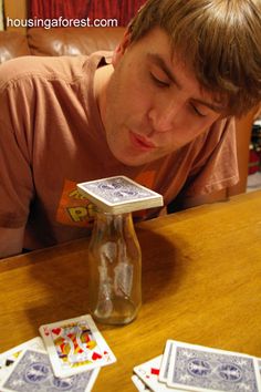 a man looking down at playing cards in a glass bottle on a table next to him