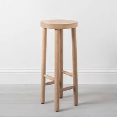 a wooden stool sitting on top of a hard wood floor next to a white wall