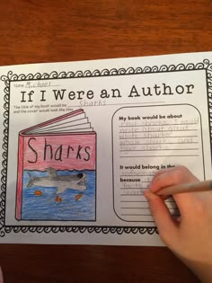 a person is holding a pencil and writing on a book with sharks in the background