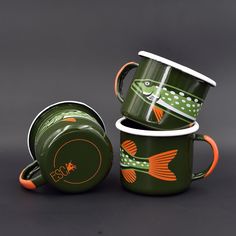 two green coffee mugs with orange handles and fish designs on them, sitting next to each other