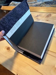 a person holding an open book on top of a wooden table