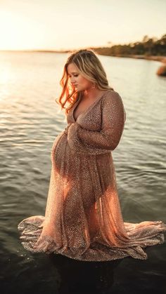 a pregnant woman standing in the water at sunset