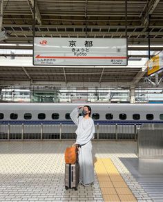 a woman standing in front of a train at a station with her hand on her head