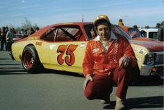 a man sitting on the ground next to a yellow race car in a parking lot