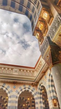 the inside of an ornate building with arches and lights on it's sides, under a cloudy blue sky