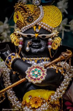 an idol is dressed in black and gold with pearls on its head, surrounded by flowers