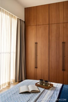 an open book on a bed in a room with wooden closets and curtains behind it