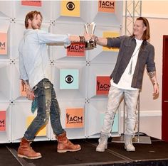 two men standing on top of a stage holding trophies