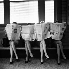 three women sitting on a bench reading newspapers while holding their heads in the same direction