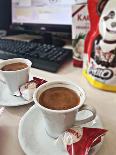 two cups of coffee sitting on top of a white saucer next to a computer keyboard