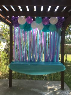 an outdoor swing with balloons and streamers attached to the back wall is decorated for a birthday party