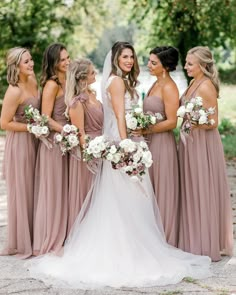 a group of women standing next to each other wearing dresses and holding bouquets in their hands