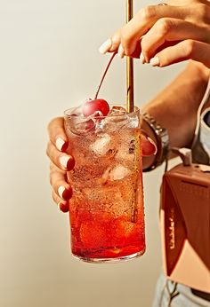 a woman holding a glass with a cherry on it and a straw in her hand