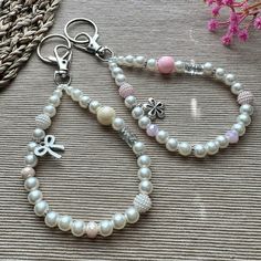 a white bracelet with charms and beads on a table next to a pink flower bouquet