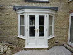 a white double door with two windows in front of a brick wall and stone walkway