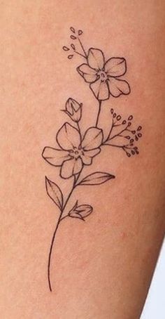 a small flower tattoo on the back of a woman's thigh, with leaves and flowers