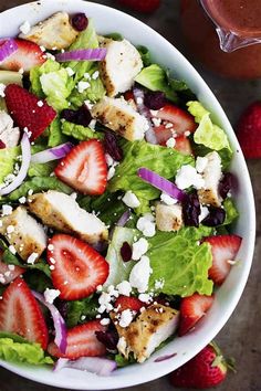 a salad with strawberries and chicken on it in a bowl next to sliced apples