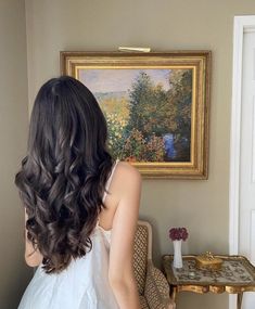 a woman standing in front of a painting looking at her reflection on the wall behind her