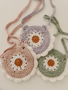 four crocheted flower purses on a white surface with one being held by a string