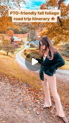 a woman standing on top of a dirt road next to a tree filled hillside with fall leaves