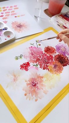 someone is painting flowers on paper with watercolors