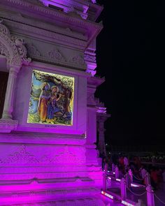 a large painting on the side of a building with purple lights in front of it