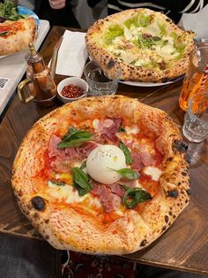 two pizzas sitting on top of a wooden table next to glasses and plates filled with food