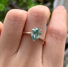 a woman's hand holding a ring with an aqua green stone on it and the middle finger