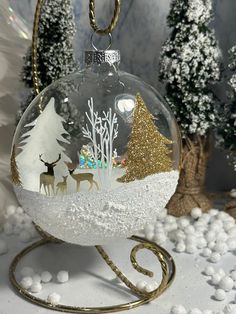 a glass ornament with deer and trees in it on a stand surrounded by snow