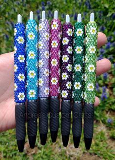 four different colored pens with flowers on them in front of some grass and blue flowers