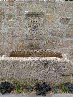 a stone fountain in front of a brick wall with plants growing on the sides and around it