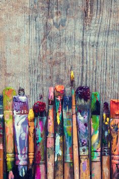 many different colored paint brushes lined up on a wooden surface with one brush in the middle