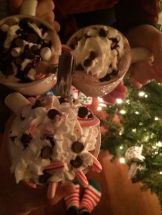 two people holding ice cream sundaes in front of a christmas tree