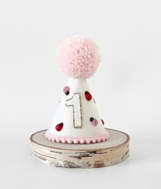 a white hat with pink pom - poms on top of a piece of wood