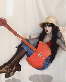 a woman sitting on the ground with a guitar in her lap and hat over her head