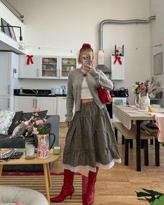 a woman taking a selfie in the kitchen while wearing a plaid skirt and red boots