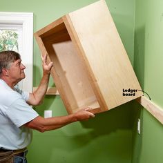 a man holding up a wooden box in the corner of a room with green walls