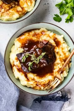 two bowls filled with mashed potatoes covered in gravy and garnished with herbs