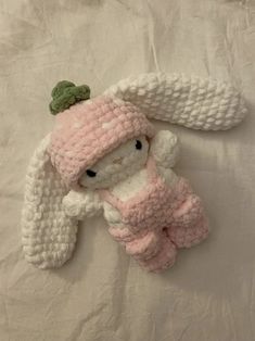 a crocheted stuffed animal laying on top of a white bed sheet with a pink hat and scarf