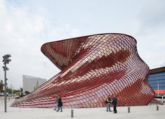 two people are standing in front of a large red structure that looks like a wave