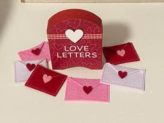 there is a small red box with hearts on it and some pink envelopes next to it