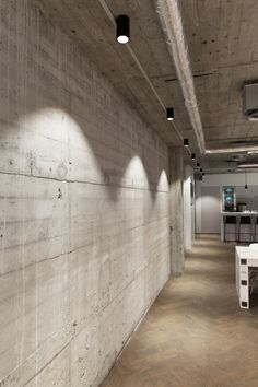 an empty room with white tables and chairs on the floor in front of a concrete wall