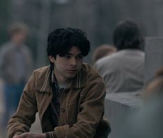 a young man sitting on a bench in front of other people