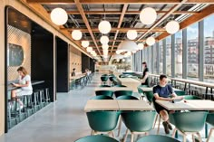 people are sitting at tables in an open area with lots of windows and green chairs