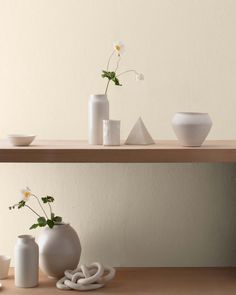 three white vases with flowers in them on a wooden shelf next to other items