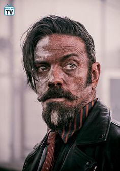 a man with a beard and moustache looks at the camera while wearing a leather jacket