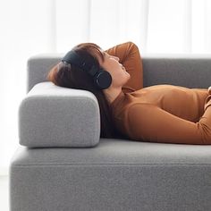 a woman laying on top of a gray couch wearing headphones with her eyes closed