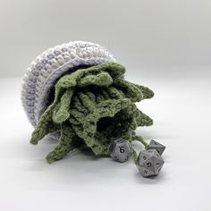 a pile of green crocheted cloth next to two metal dices on a white surface